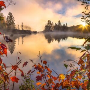 Mist and steam rise from the surface of a small pond in Northern Vermont. Vibrant reds